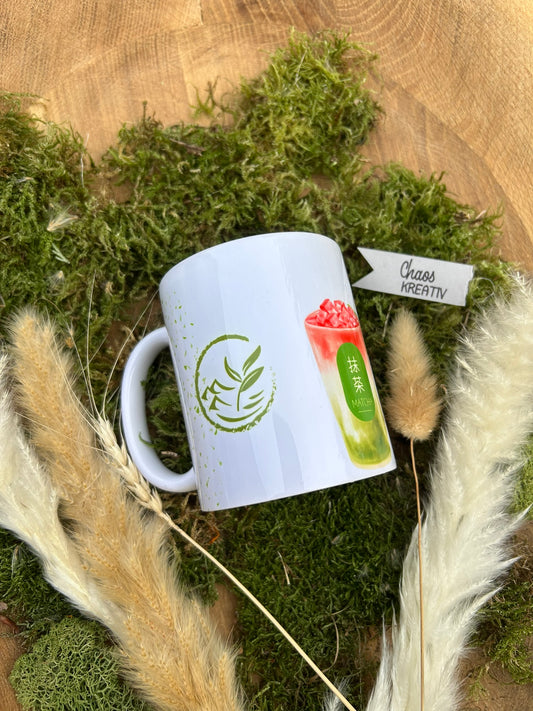 Weiße Keramiktasse mit grünem Matcha-Motiv und farbigem Matcha-Drink-Print, auf Moos liegend